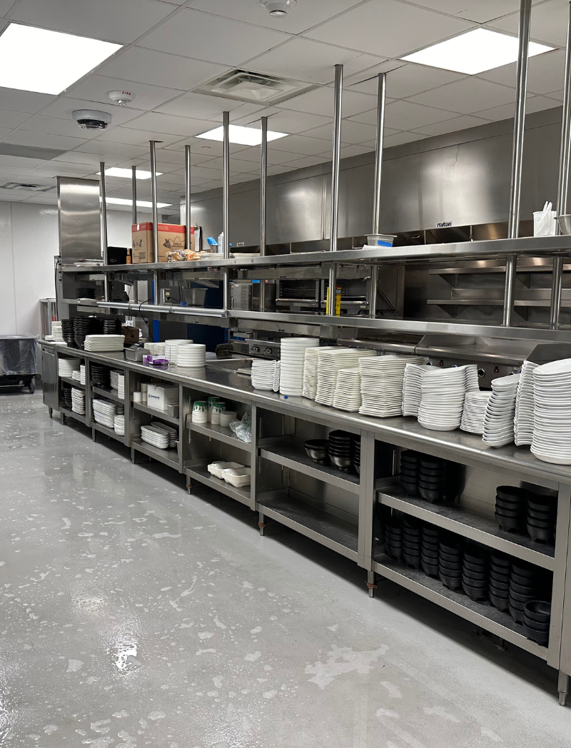 A restaurant kitchen with a lot of shelves and plates on them. The floor is wet from being recently washed