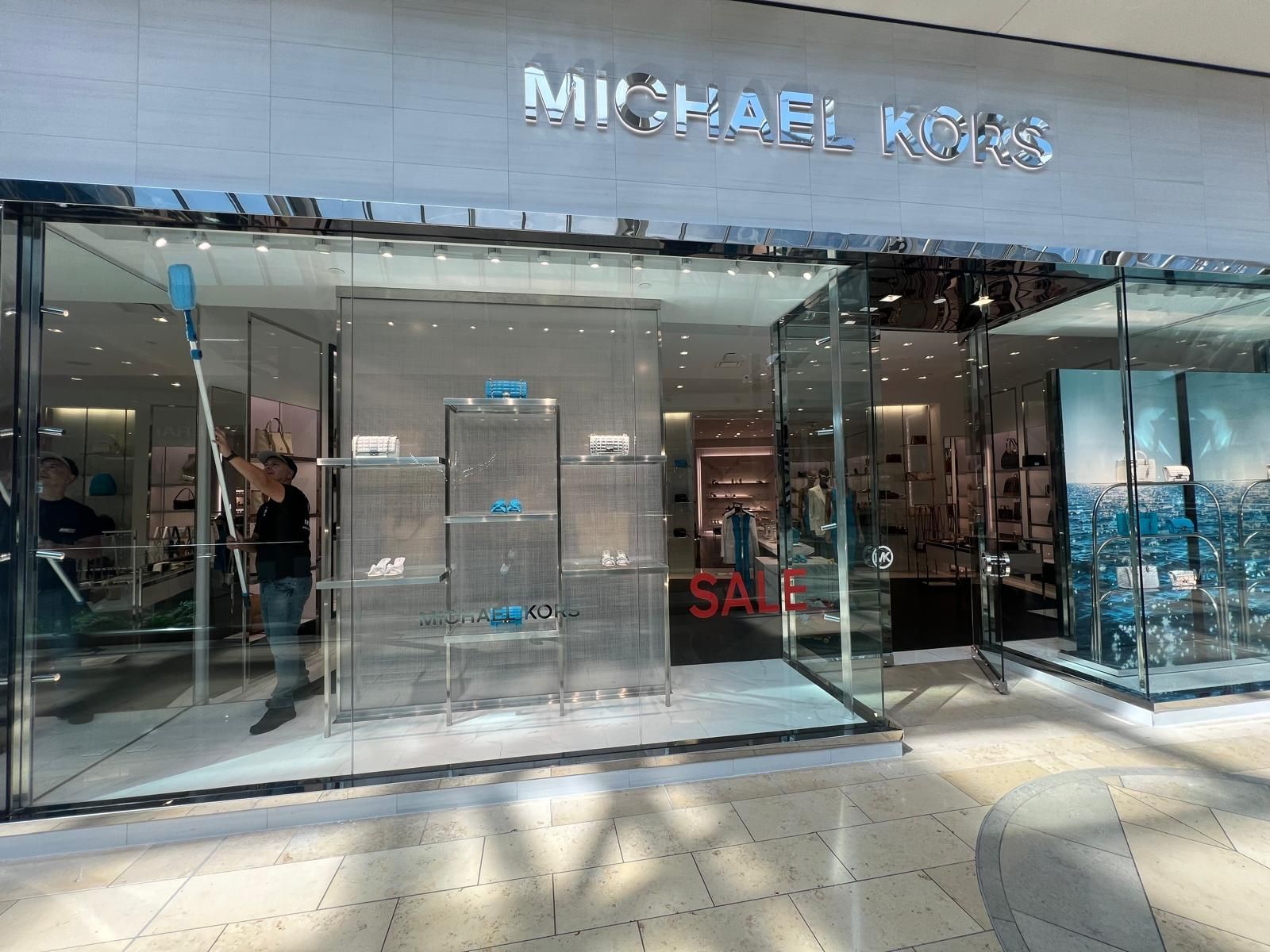 A man is cleaning the windows of a michael kors store.