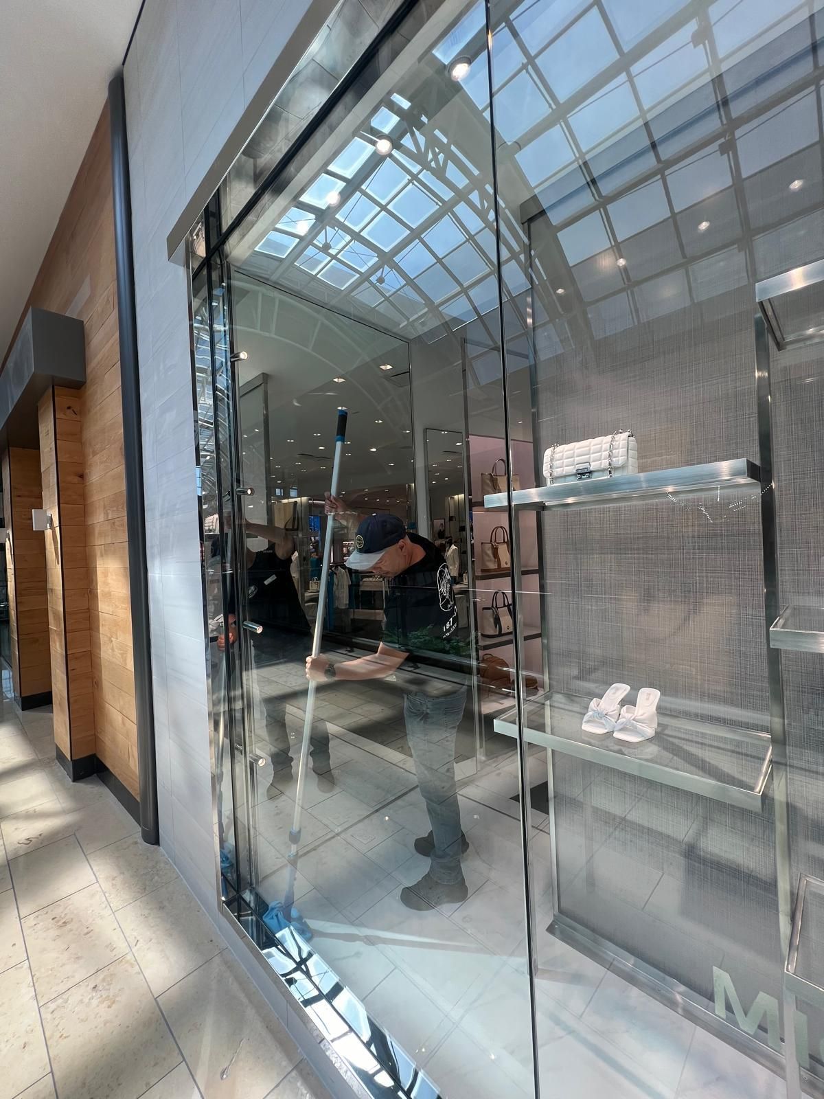 A man is cleaning a store window with a mop.