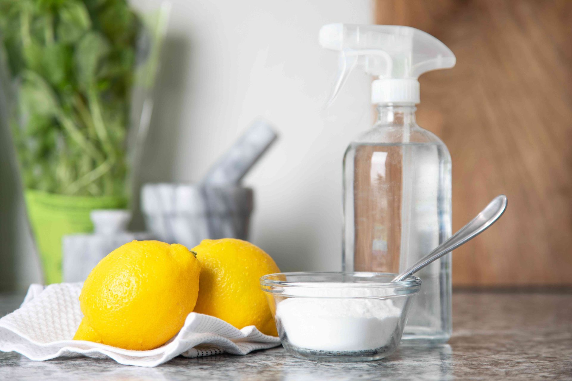 A spray bottle , a bowl of baking soda , and lemons on a counter.