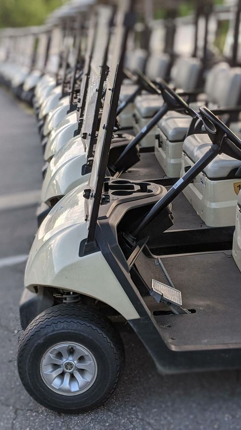 A row of golf carts are parked in a parking lot.