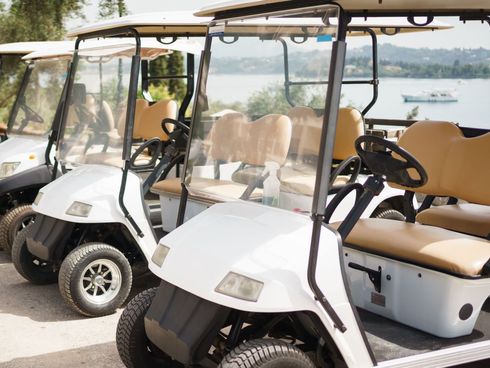 A row of golf carts are parked next to each other in a parking lot.