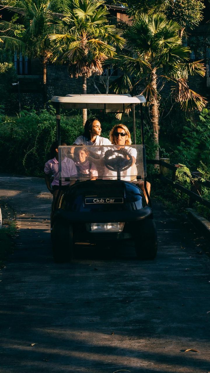 A group of people are riding in a golf cart down a dirt road.