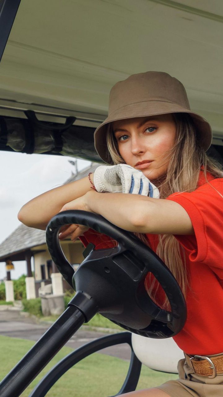 A woman wearing a hat and gloves is sitting in a golf cart.
