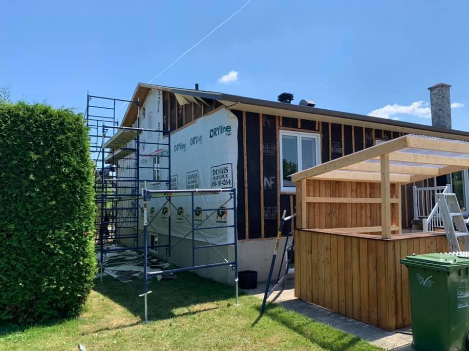Une maison est en construction avec un échafaudage et une poubelle verte devant.