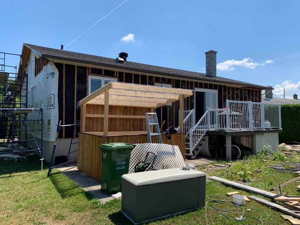 Une maison est en cours de rénovation avec un hangar en bois dans l'arrière-cour.