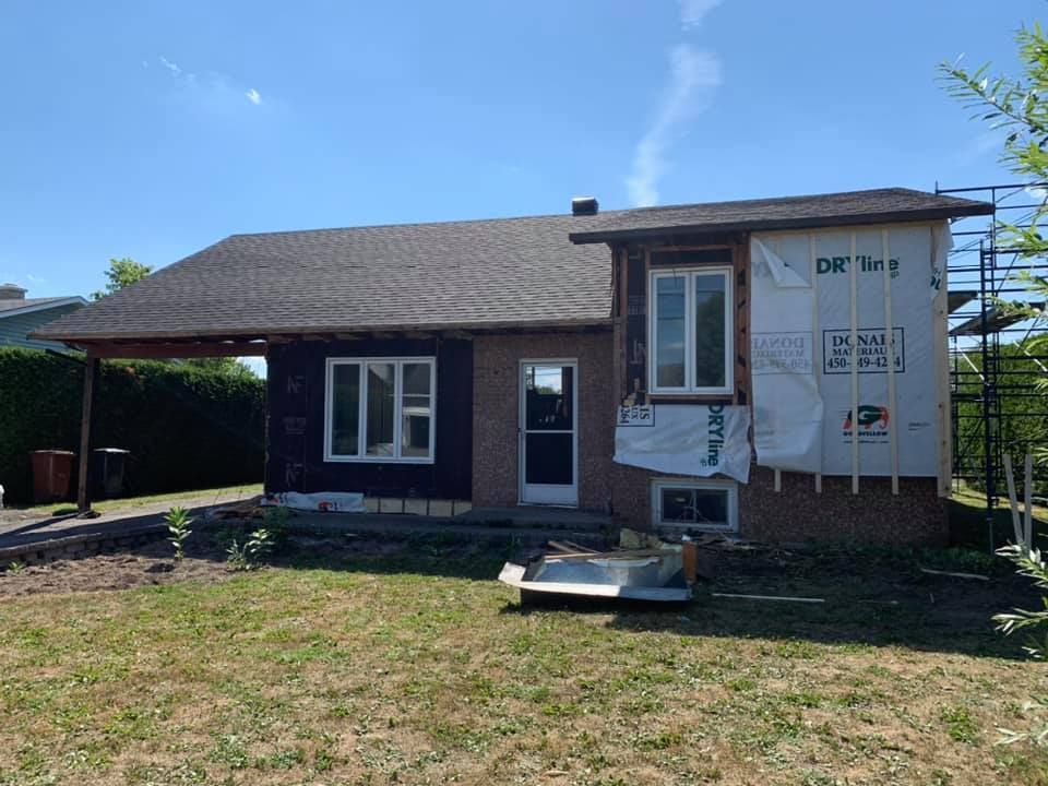 Une petite maison avec beaucoup de fenêtres se trouve au milieu d'un champ herbeux.