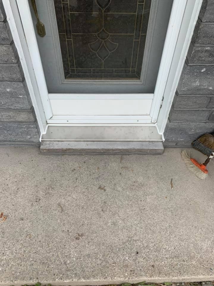 Une porte blanche avec un vitrail se trouve sur un porche en béton.