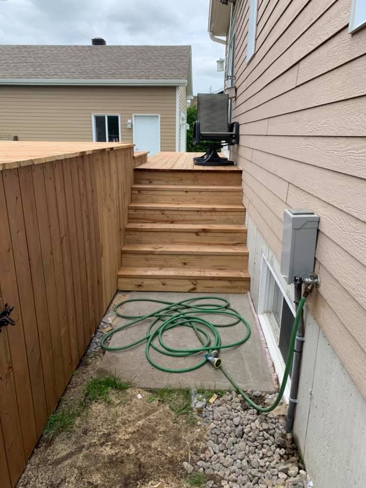 Un tuyau est posé sur le côté d'une maison à côté d'une terrasse en bois.