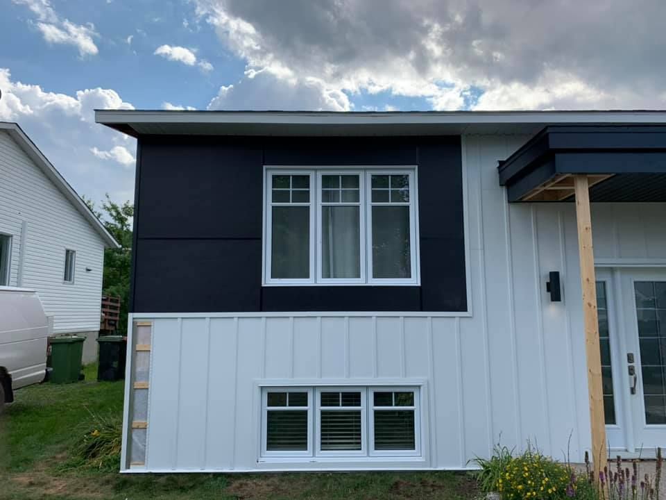 Une maison blanche avec un revêtement noir et une fenêtre.