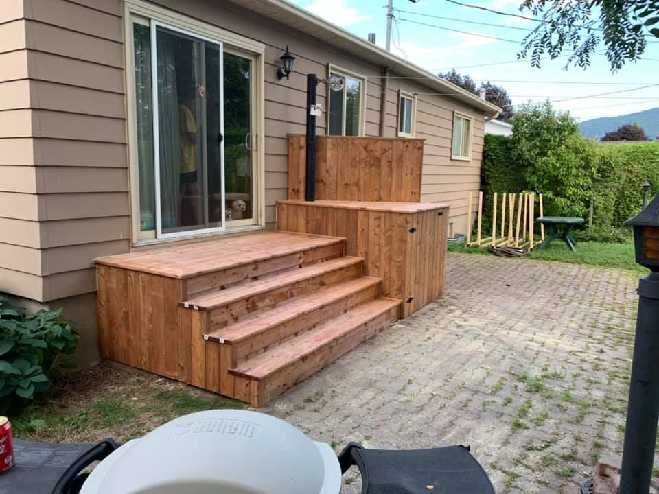 Une terrasse en bois avec des escaliers se trouve devant une maison.