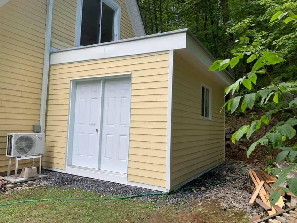 Une maison jaune avec un hangar blanc attaché.