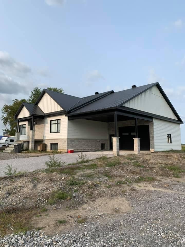 Une grande maison blanche avec un toit noir est assise au sommet d'un champ de terre.