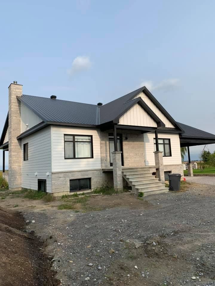 Une maison blanche avec un toit noir est assise au sommet d'un champ de terre.
