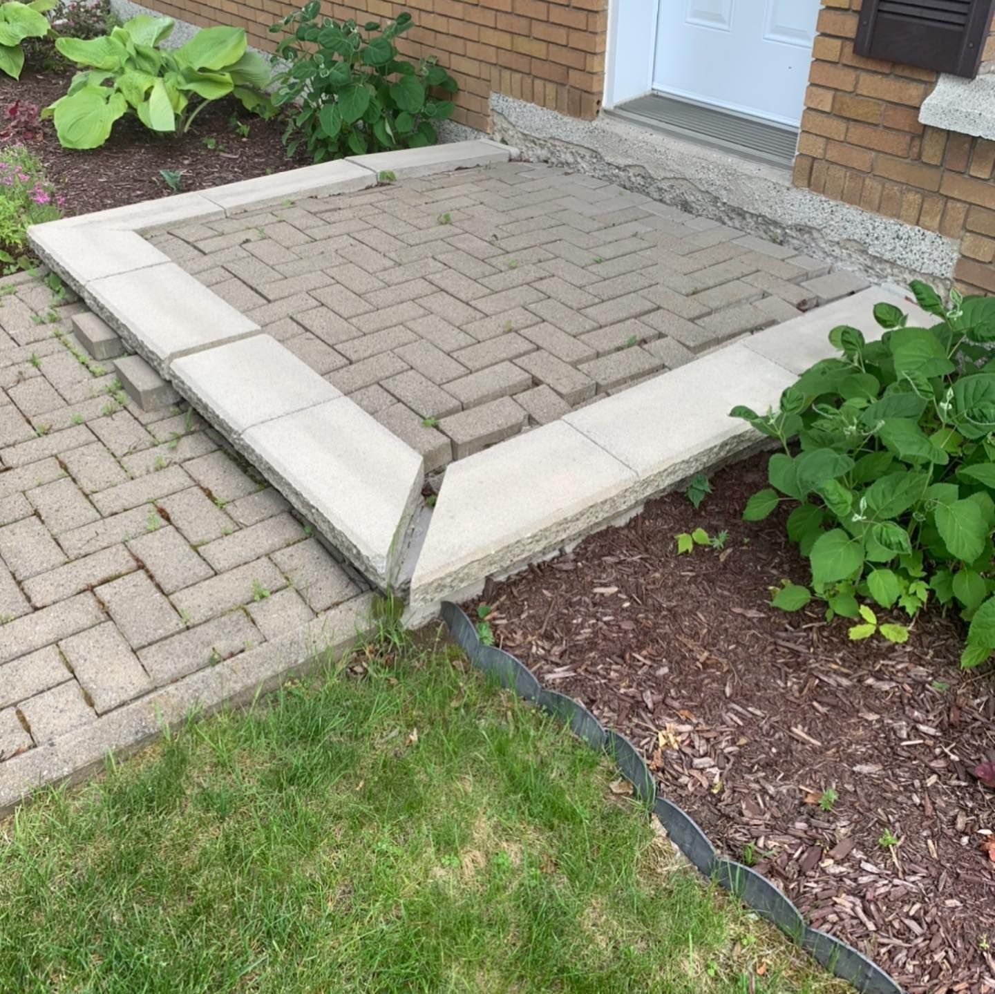 Une allée en briques avec des marches menant à une porte devant une maison en briques.