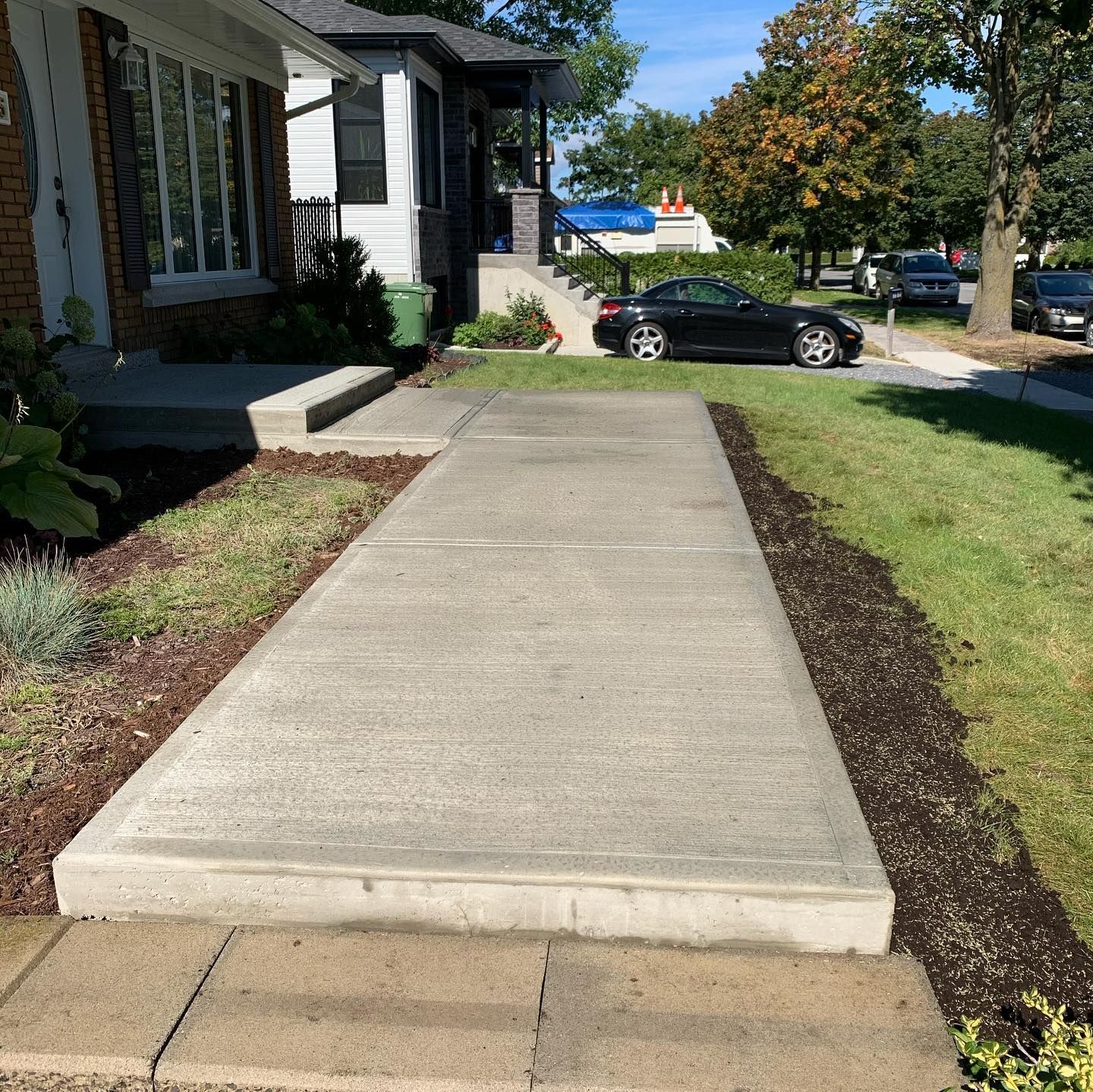 Une passerelle en béton menant à une maison avec une voiture garée sur le côté.