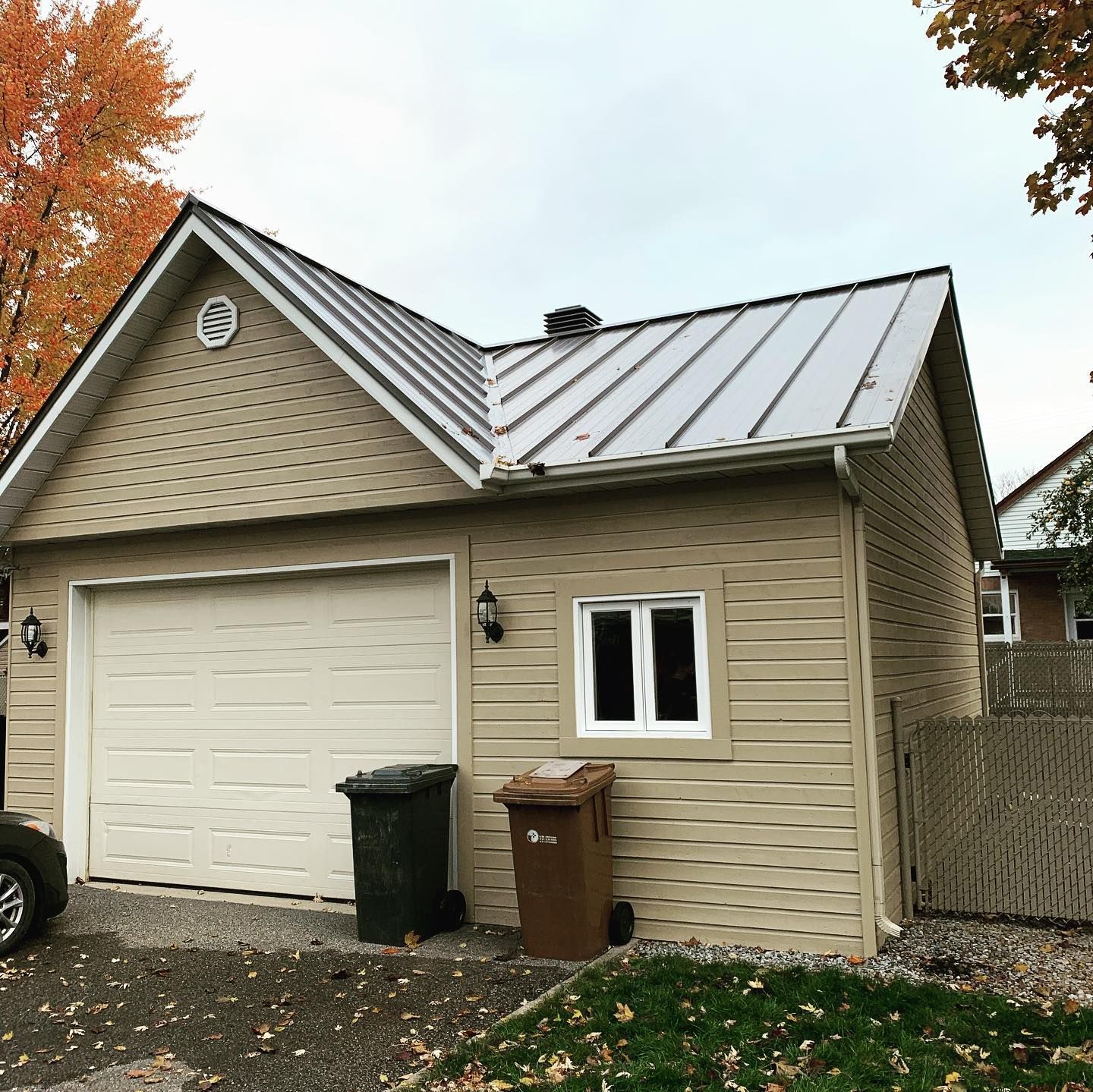 Une petite maison avec un garage et un toit en métal.