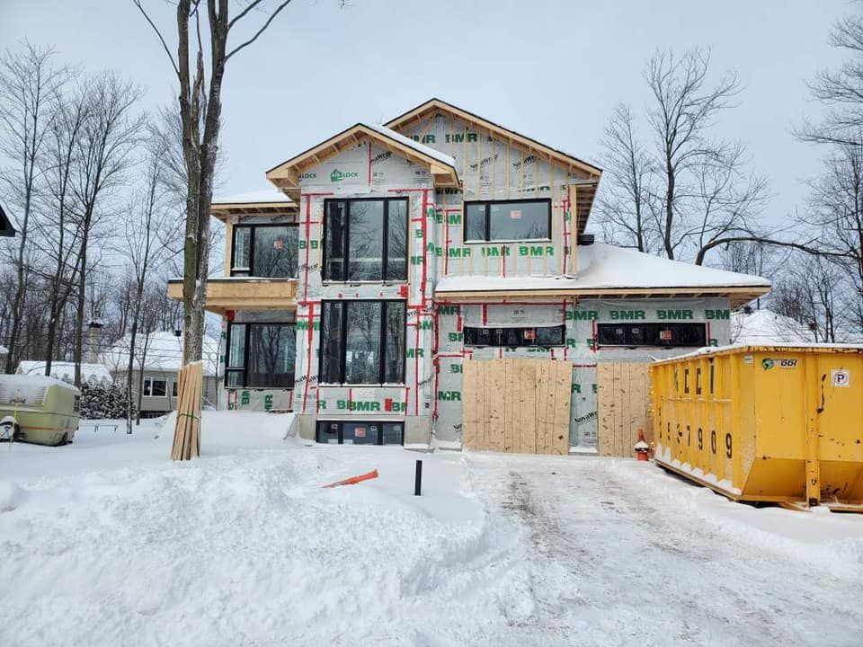 Une maison est en construction dans la neige avec une benne jaune devant elle.