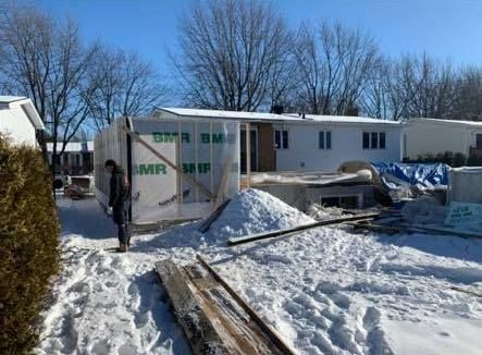 Un homme se tient debout dans la neige devant une maison en construction.