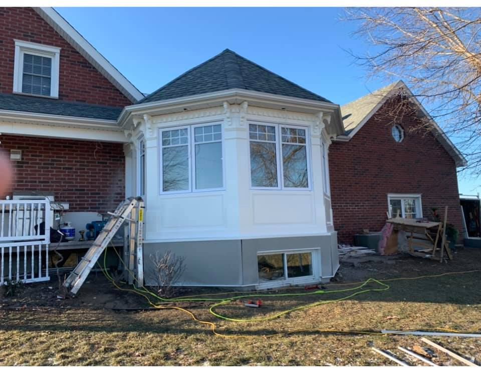 Une maison en briques avec un porche blanc et une échelle devant.