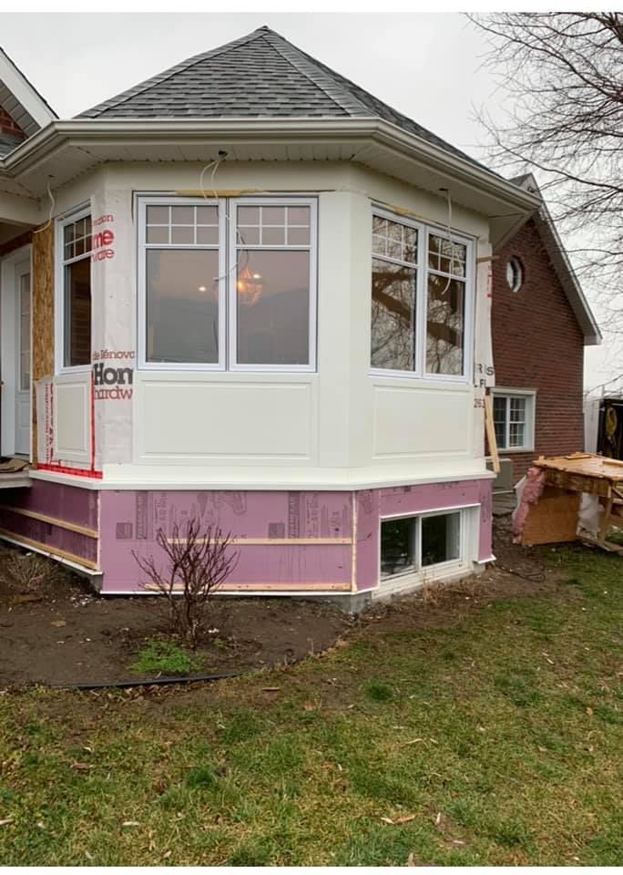 Une maison blanche avec un bâtiment en briques en arrière-plan est en cours de rénovation.