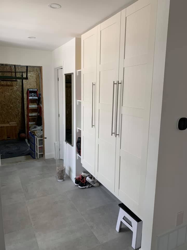 Un couloir avec des armoires blanches et un tabouret.