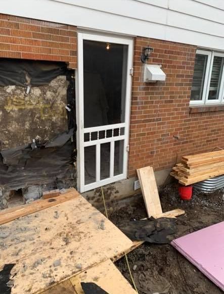 Une porte moustiquaire est en cours d'installation sur le côté d'une maison en briques.
