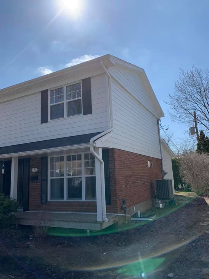 Une maison en briques avec un revêtement blanc et des volets noirs par une journée ensoleillée.