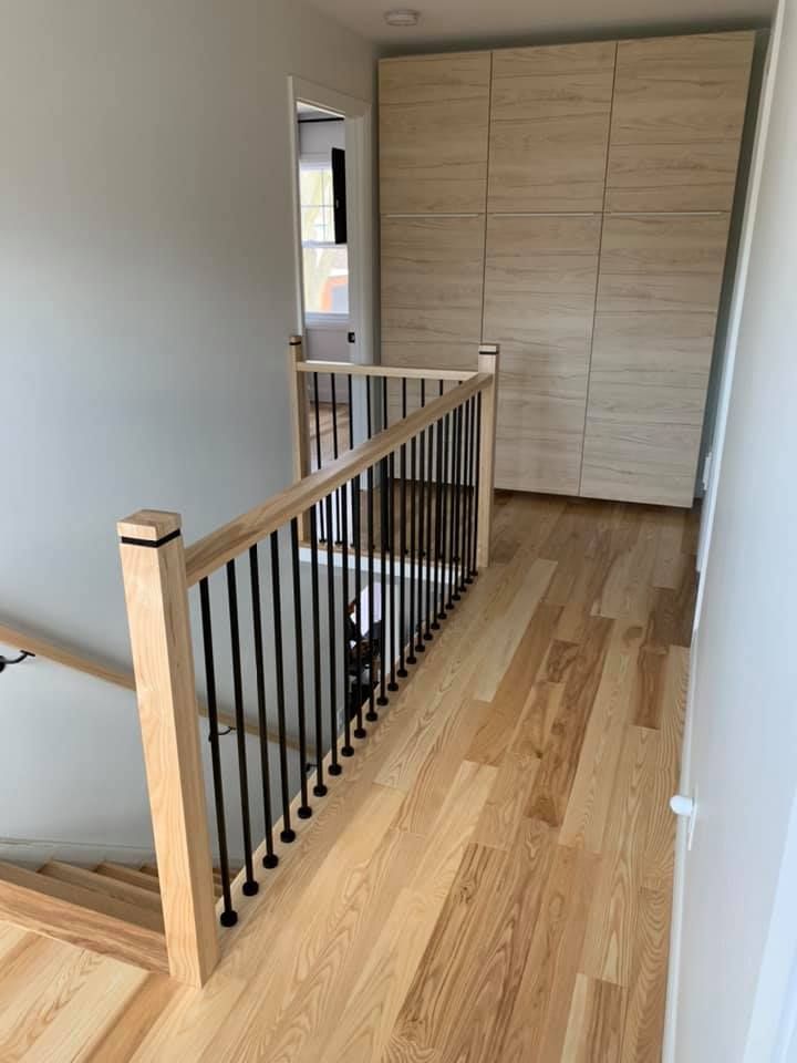 Un escalier en bois avec une rampe noire dans un couloir.