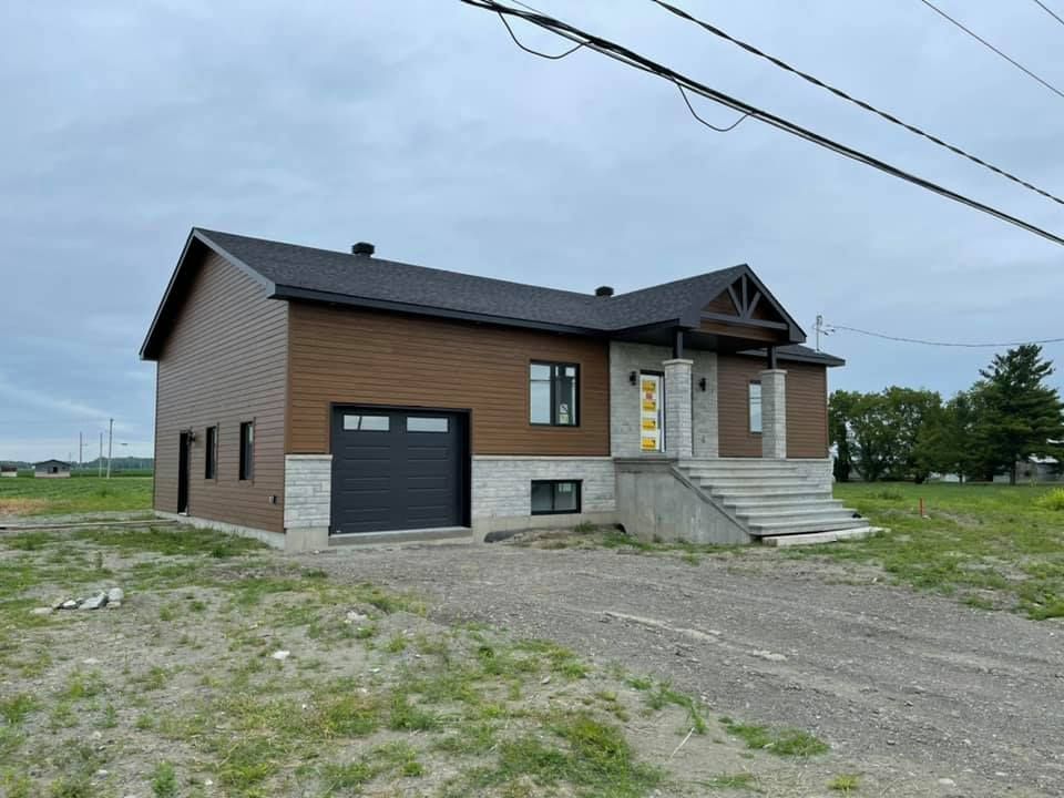 Une maison avec une porte de garage noire se trouve au milieu d'un champ herbeux.