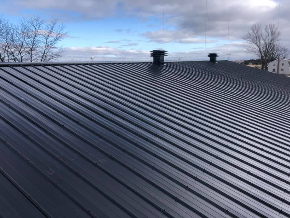 Un gros plan d'un toit en métal noir avec un ciel bleu en arrière-plan.