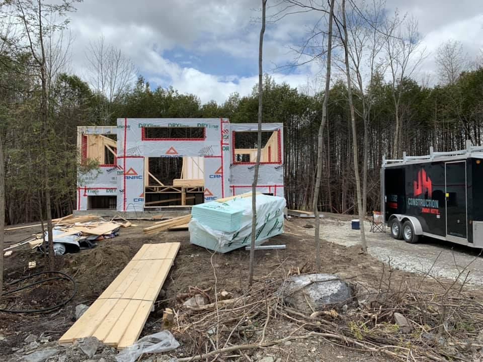Une maison est en construction dans les bois avec une caravane garée devant.