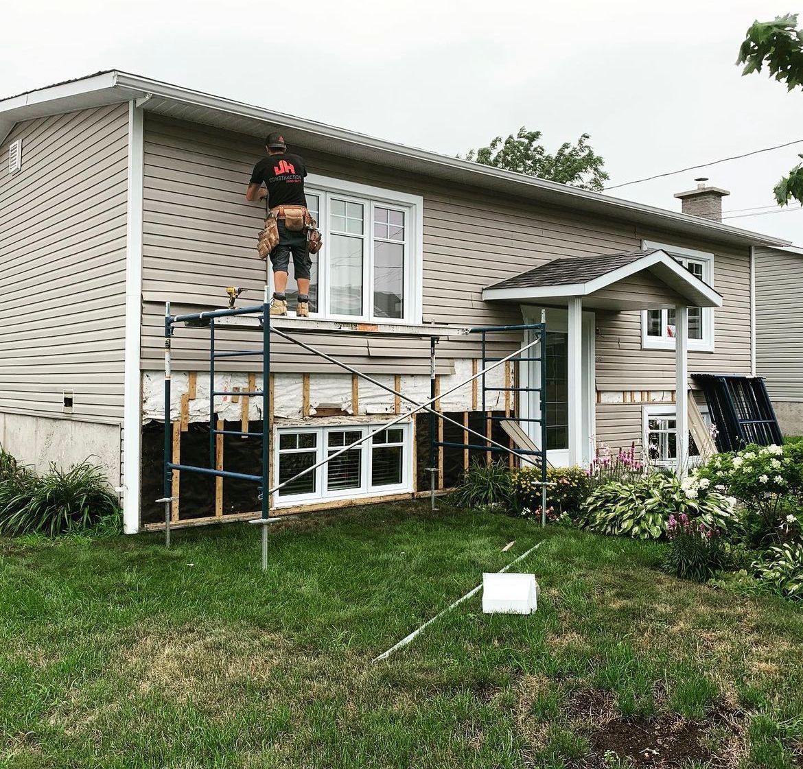 Un homme se tient sur un échafaudage devant une maison.