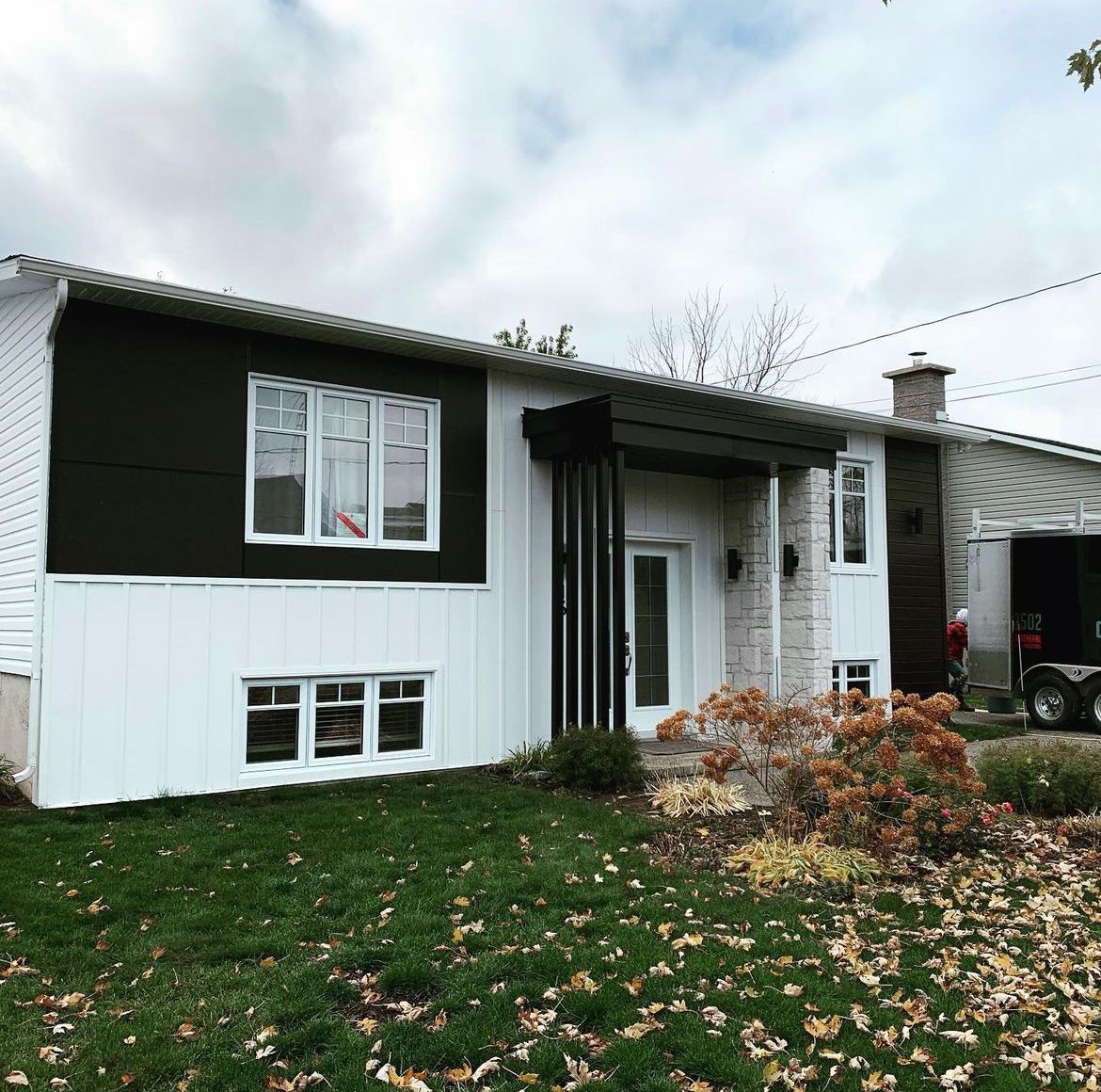 Une maison blanche avec un revêtement et des fenêtres noirs est posée sur une pelouse verte luxuriante.