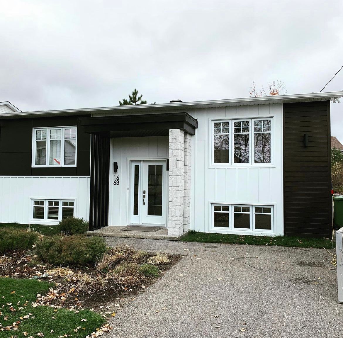 Une maison noire et blanche avec beaucoup de fenêtres et une allée en gravier.