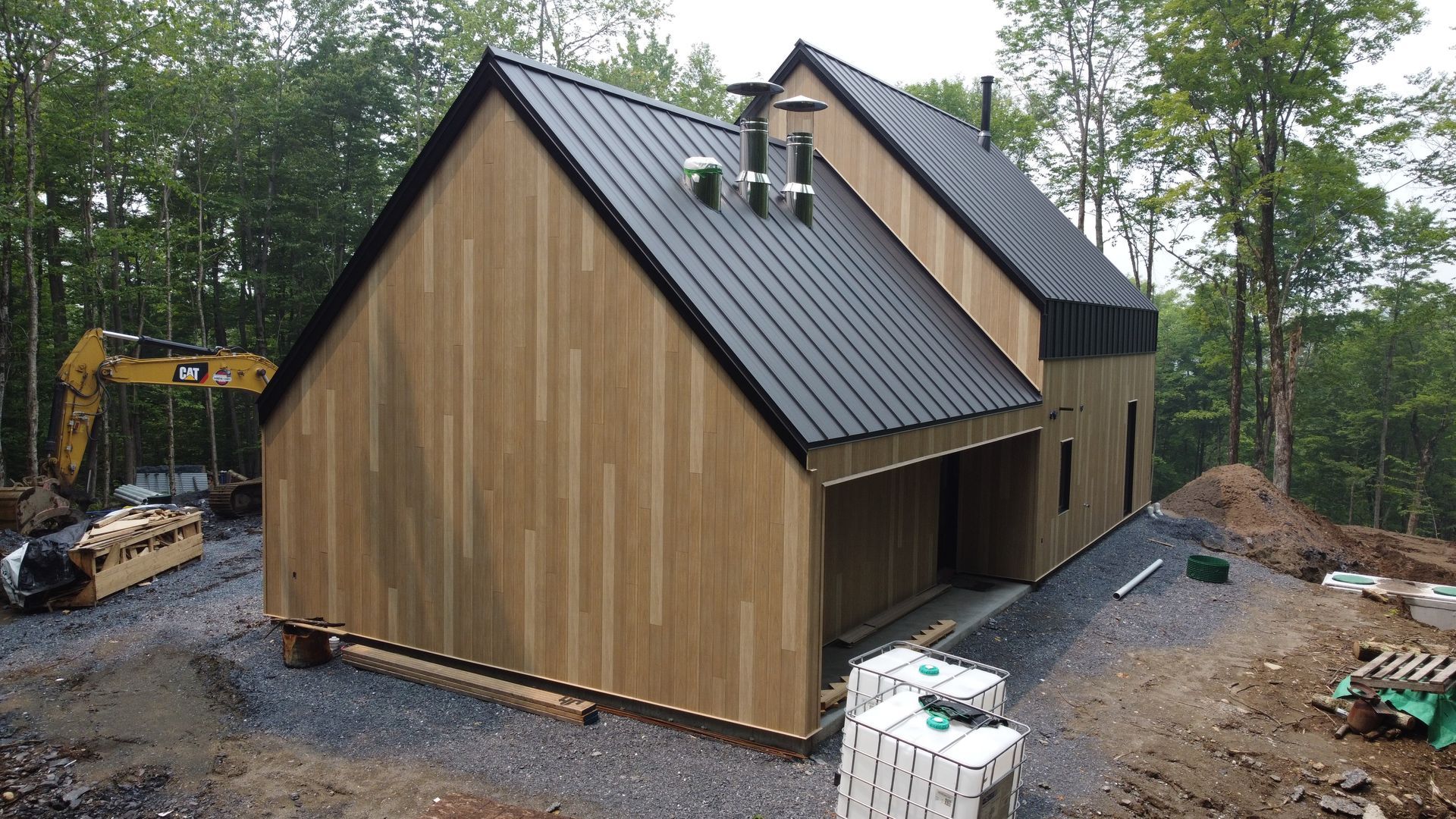 Une maison avec un toit noir est en construction dans les bois.