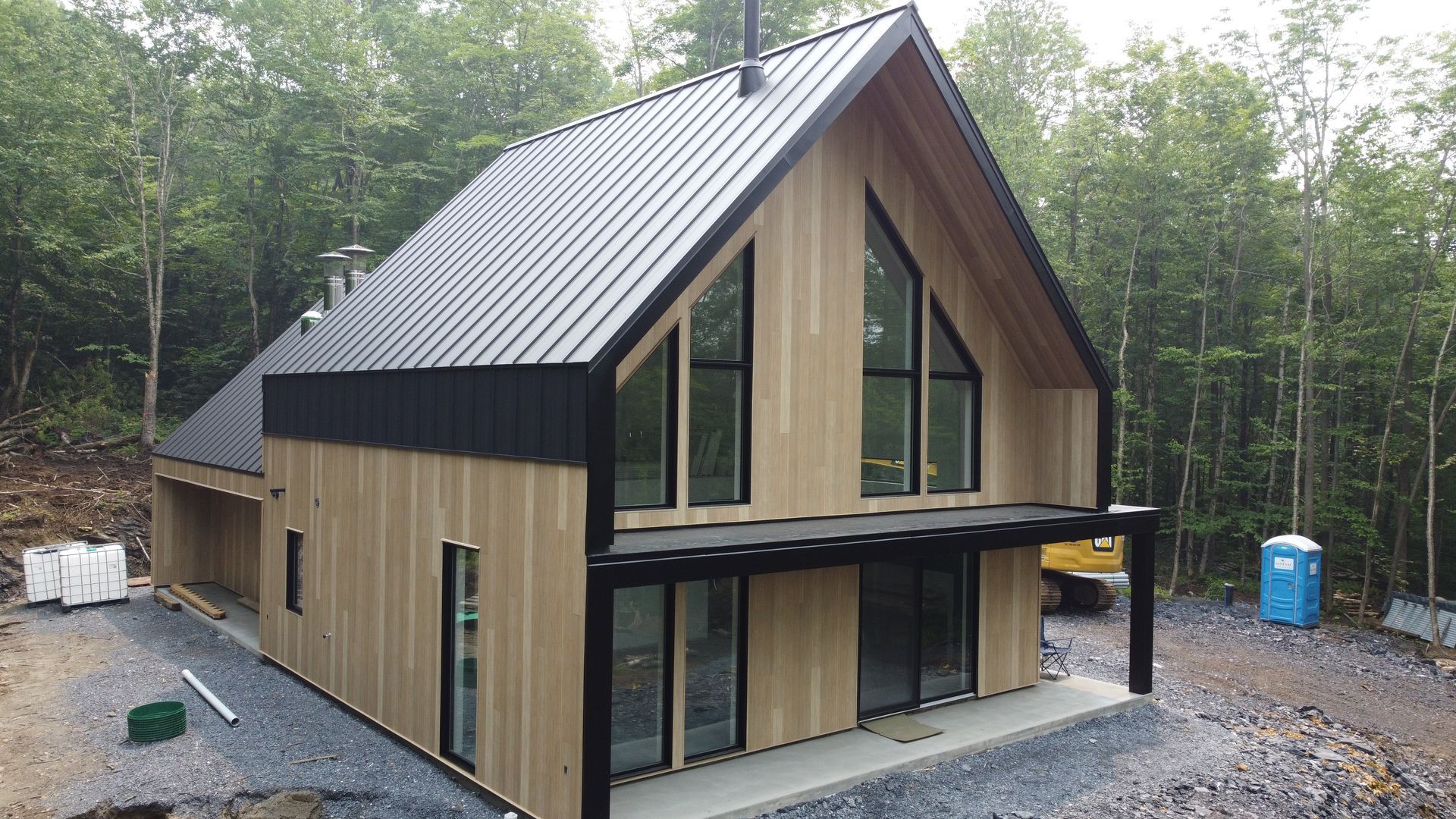 Une maison en bois avec un toit noir est en construction au milieu d'une forêt.