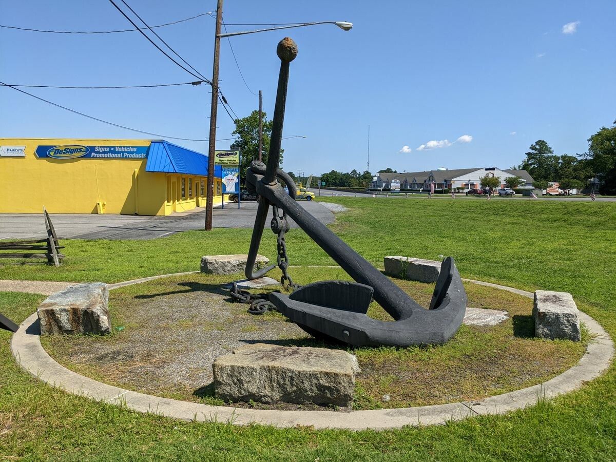 a large anchor is sitting in the grass in front of a yellow building