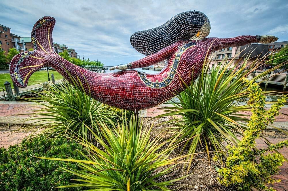 a statue of a mermaid is sitting in a garden surrounded by plants