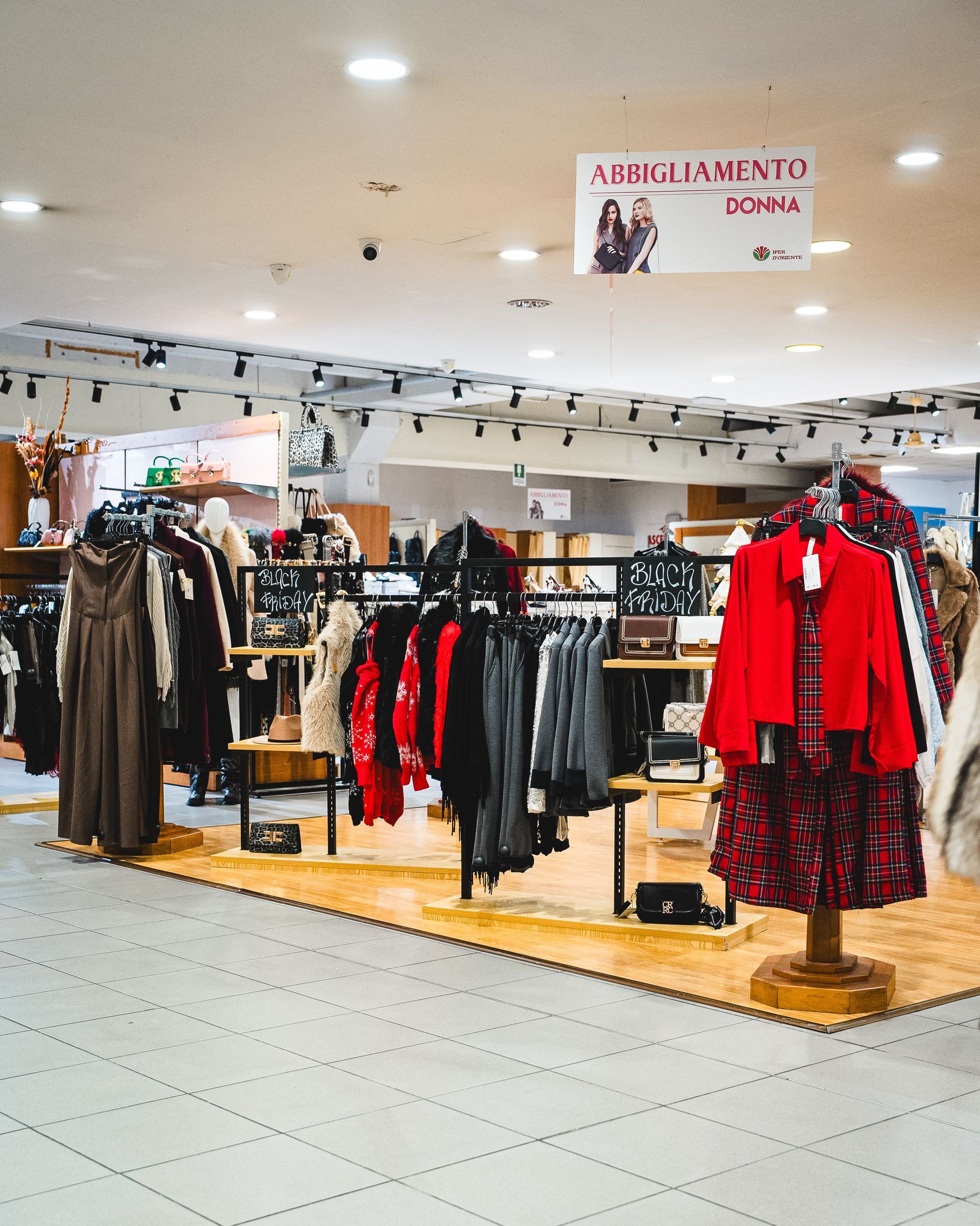 Interno di un negozio di abbigliamento con scaffali pieni di vestiti esposti, tra cui una giacca e un vestito rossi.