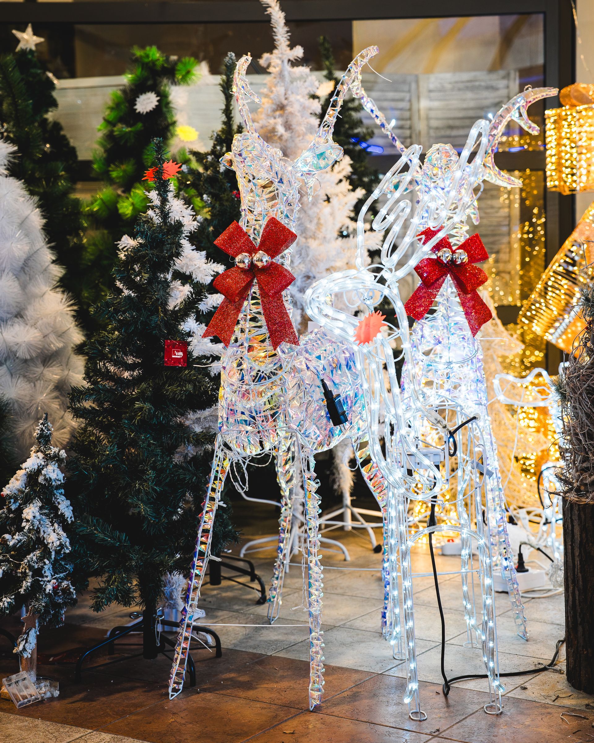Decorazioni a forma di renna illuminata con fiocchi rossi, circondate da alberi di Natale.