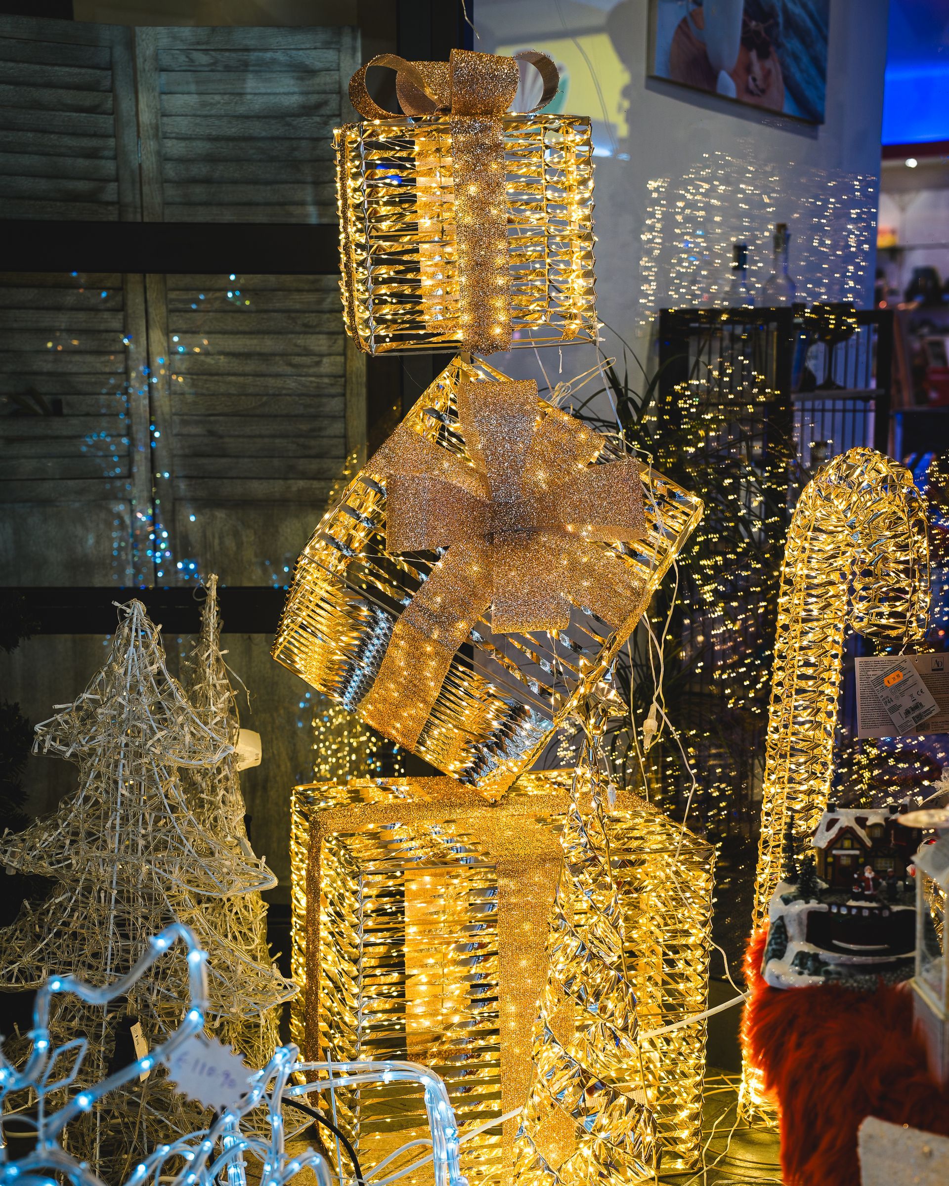 Decorazioni dorate e illuminate in scatole regalo nella vetrina di un negozio, con un albero di Natale e luci.