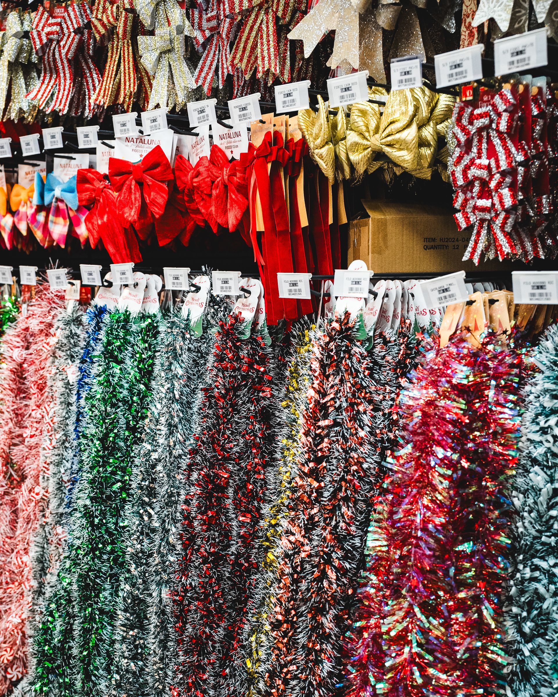 File di colorati nastri e fiocchi natalizi in un negozio, tra cui decorazioni rosse, verdi e dorate.