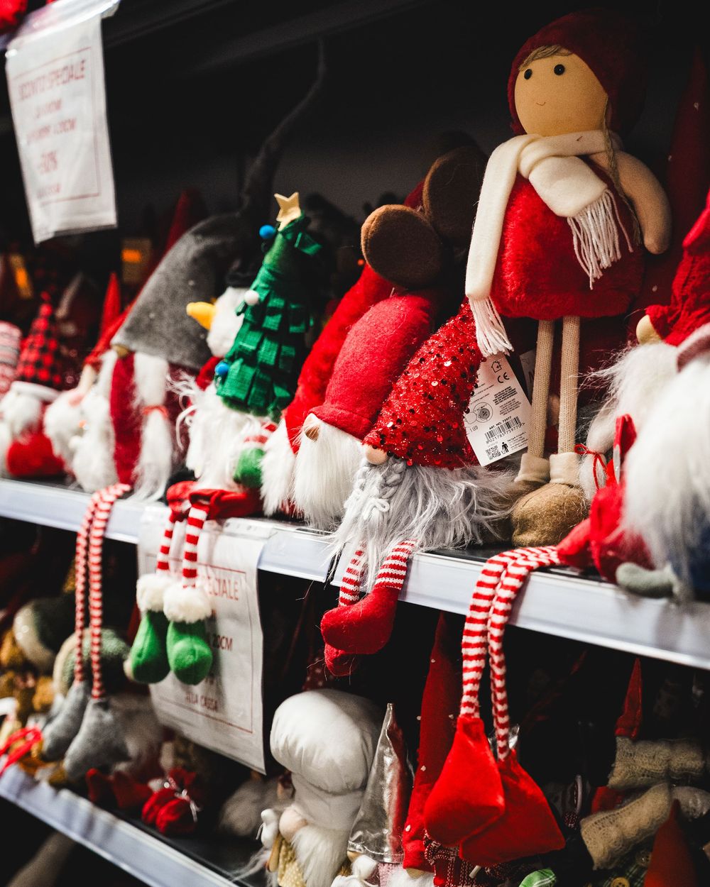 Gnomi natalizi sullo scaffale di un negozio, con cappelli e sciarpe rossi, verdi e bianchi.