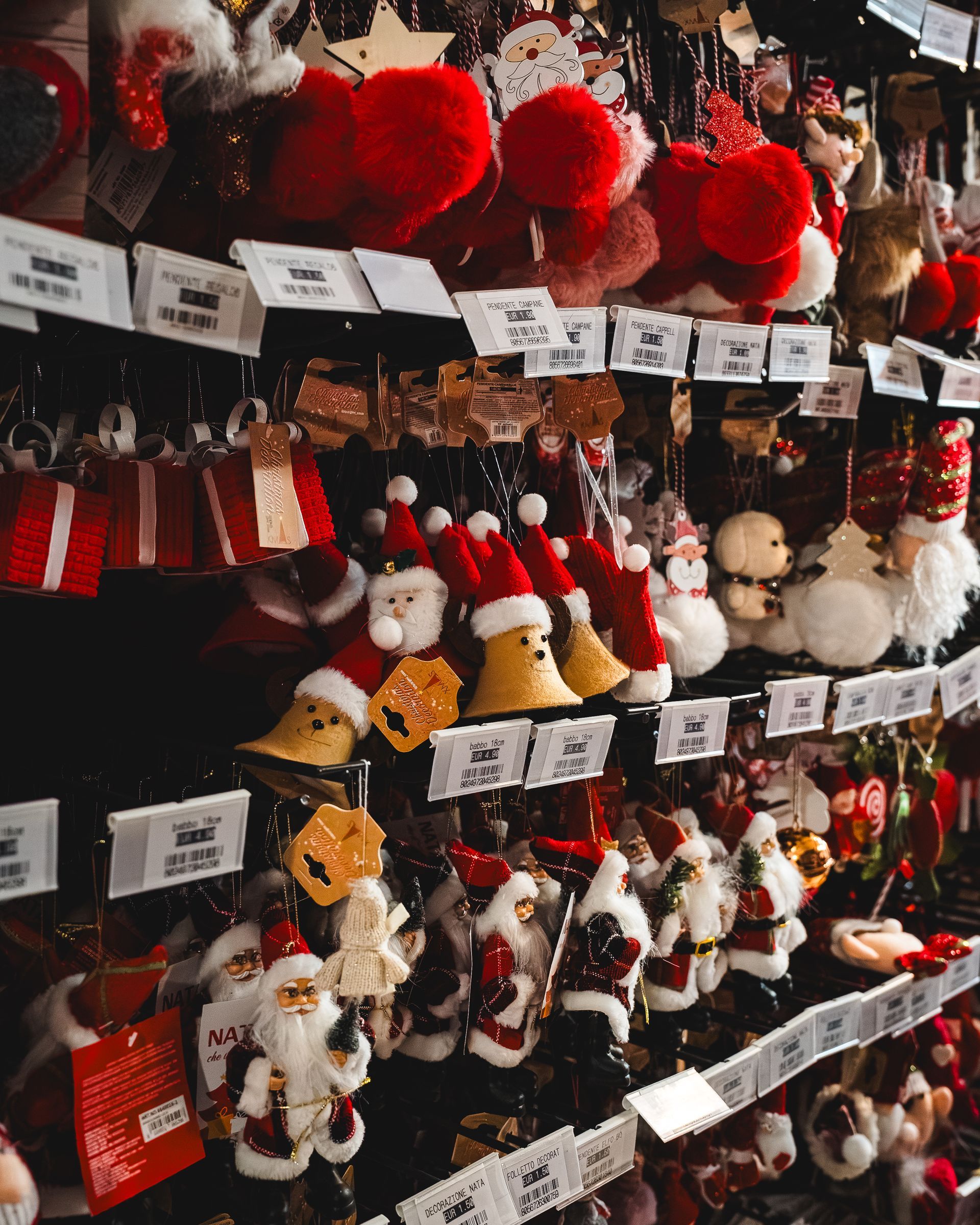 Decorazioni natalizie esposte in un negozio, tra cui figure di Babbo Natale e campanellini. Colori rosso e bianco.