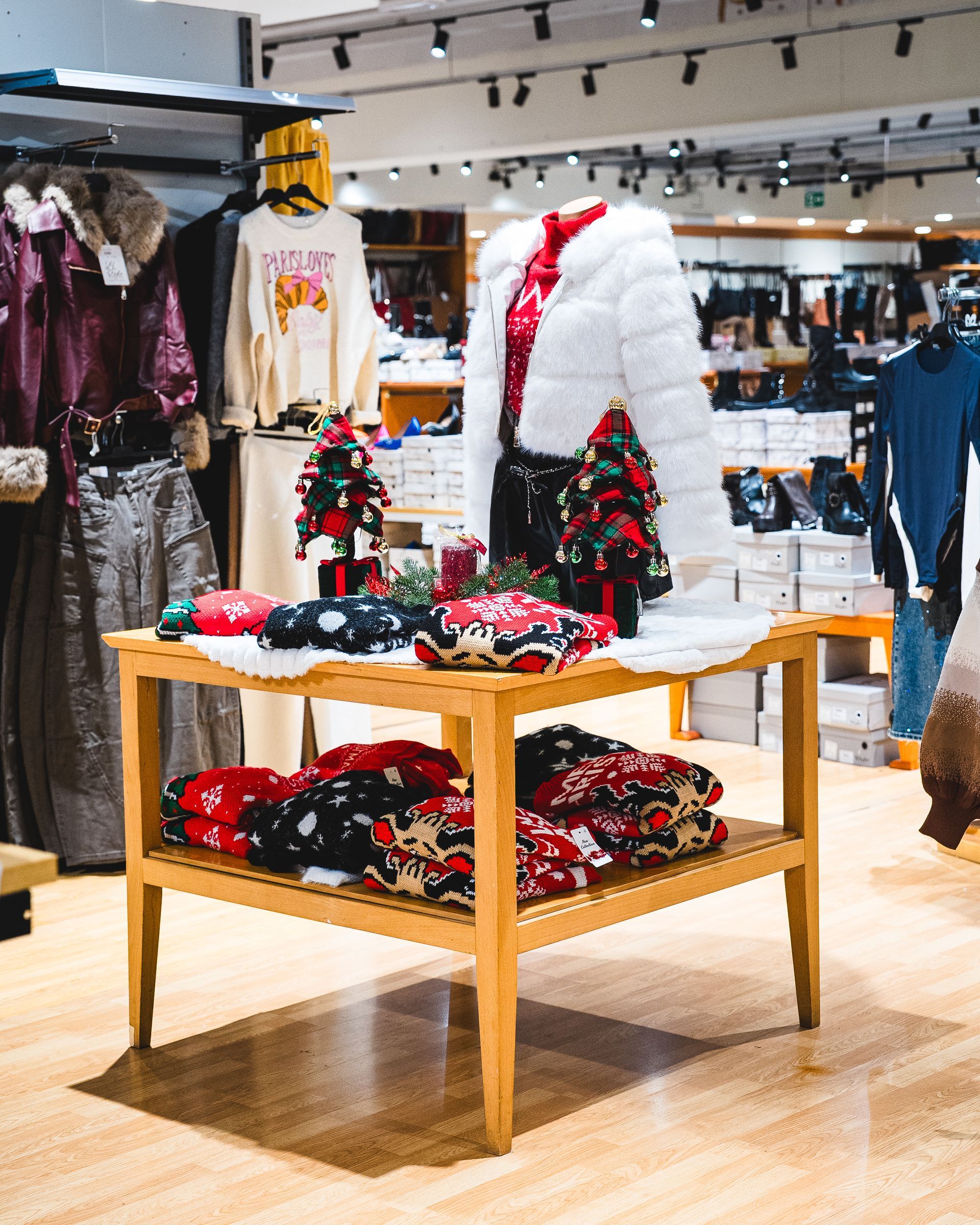 Esposizione di abiti in un negozio con un tavolo di abiti e decorazioni natalizie.