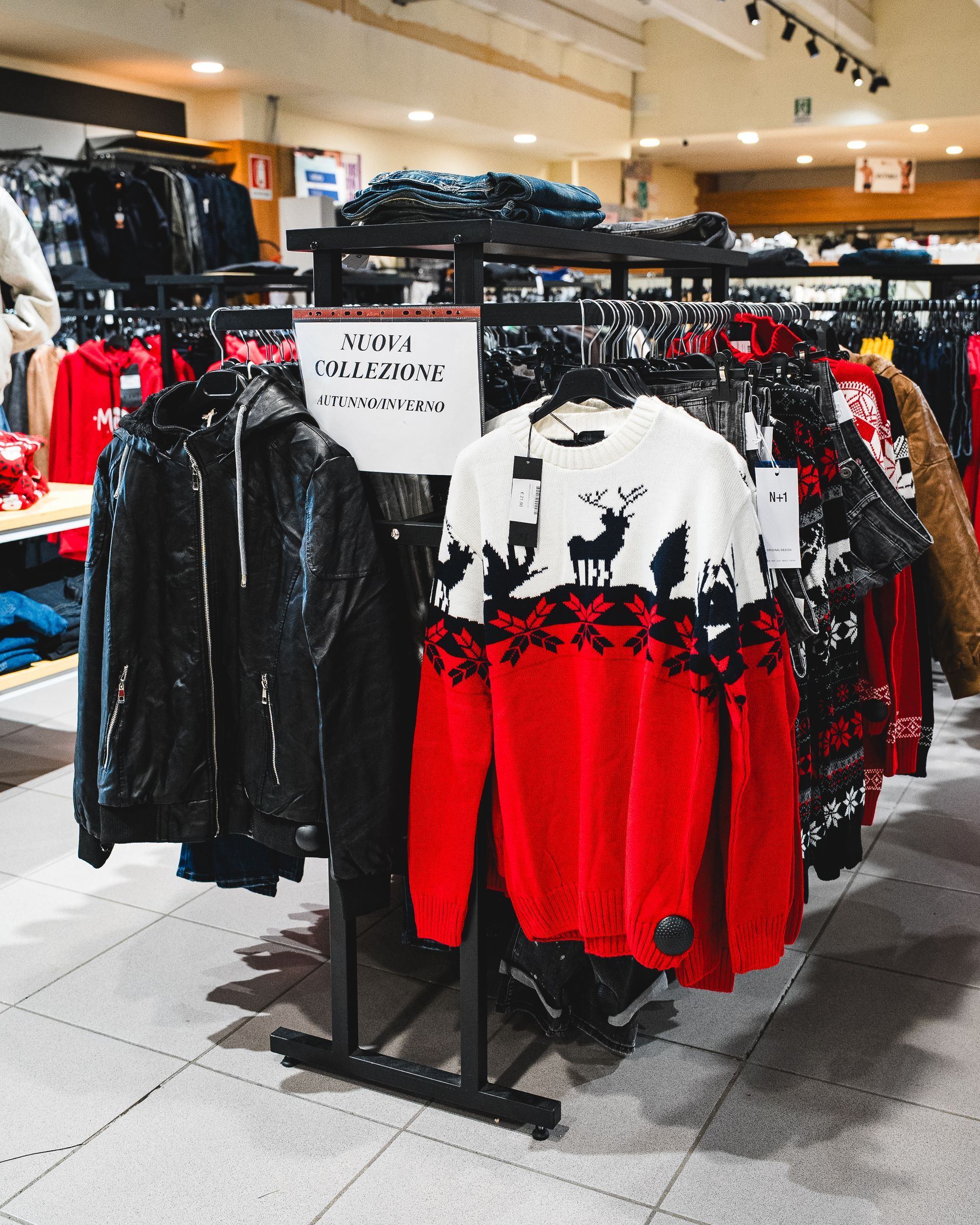 Espositori con giacche e maglioni in un negozio. Indumenti rossi, bianchi e neri in mostra.