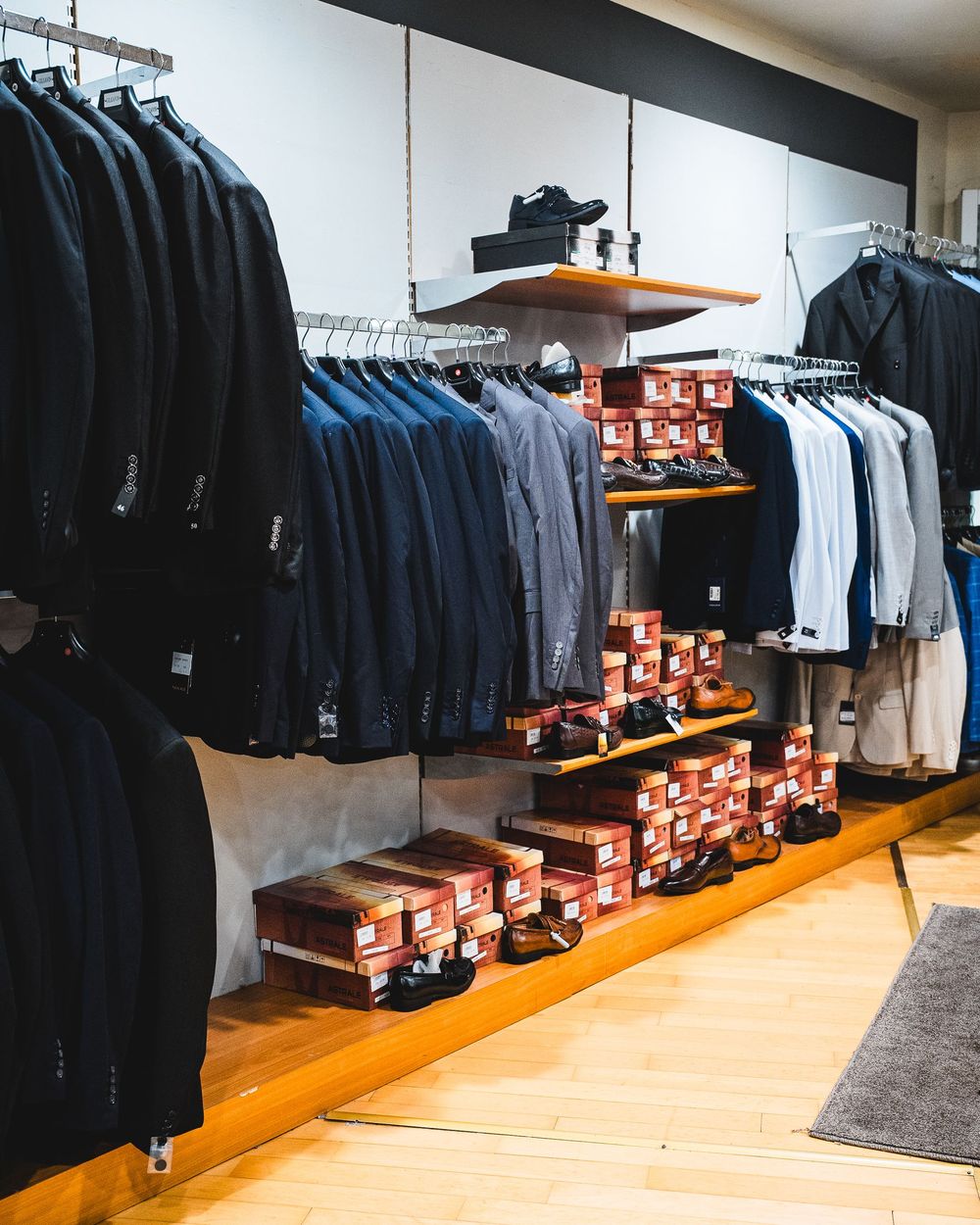 Interno di un negozio di abbigliamento con abiti e scarpe esposti su scaffali e rastrelliere.