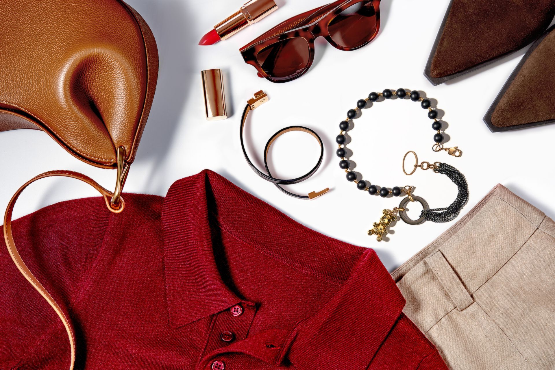 Accessori moda su sfondo bianco: borsa, maglietta rossa, occhiali da sole, gioielli, scarpe, rossetto.