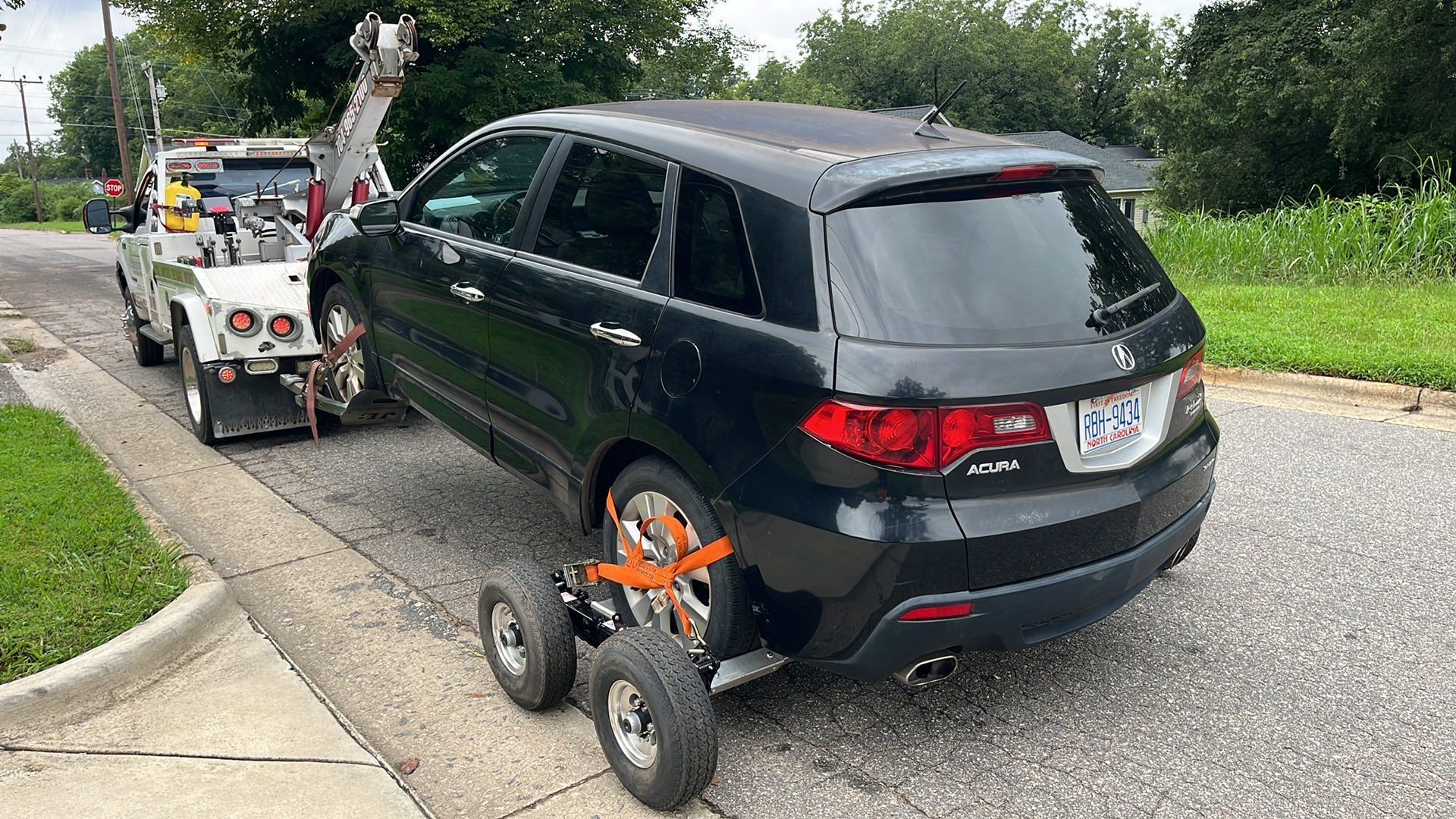 A black SUV being towed by a tow truck on a street. The SUV's rear wheels are on a dolly.